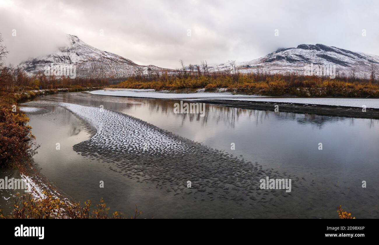 Sand bank with snow in a shallow Rapa river with snow covered mountains and autumn colors, Sarek National park, Sweden Stock Photo