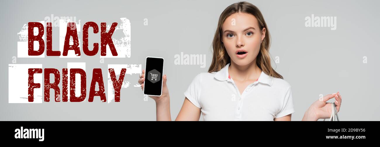 shocked woman holding smartphone near black friday lettering and cart illustration on grey, banner Stock Photo