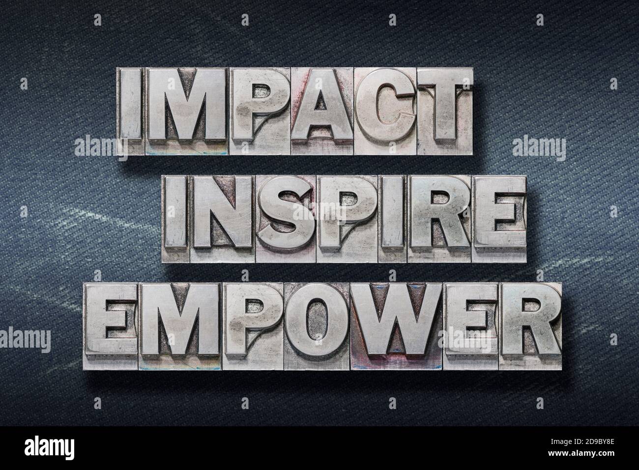 impact inspire empower words made from metallic letterpress on dark jeans background Stock Photo
