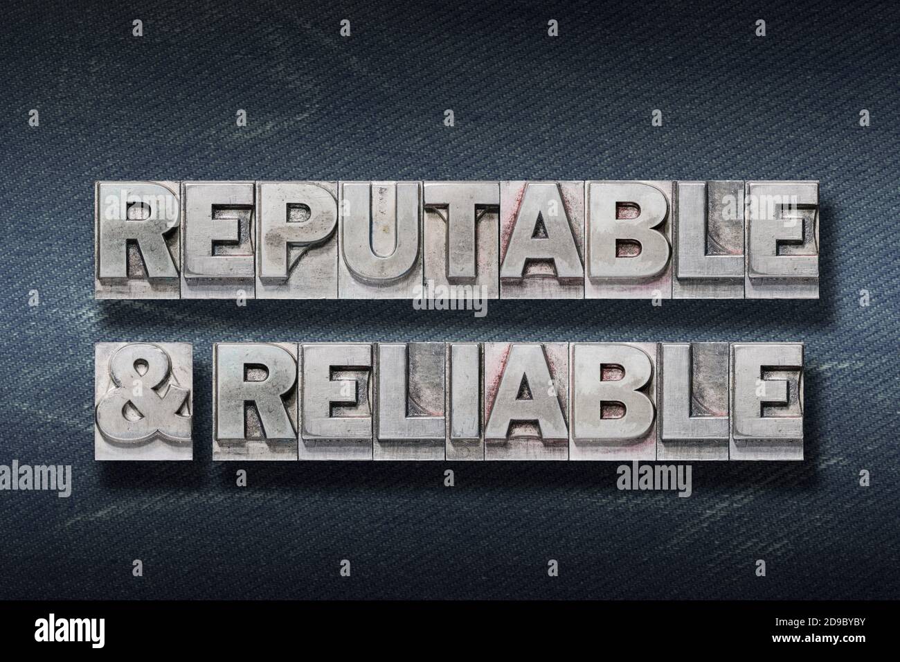 reputable and reliable phrase made from metallic letterpress on dark jeans background Stock Photo