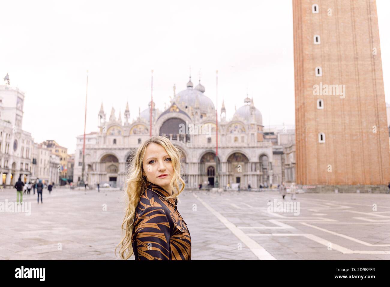 Blonde woman looking at the camera, in a long dark dress walking in Piazza San Marco, Venice, Italy Stock Photo