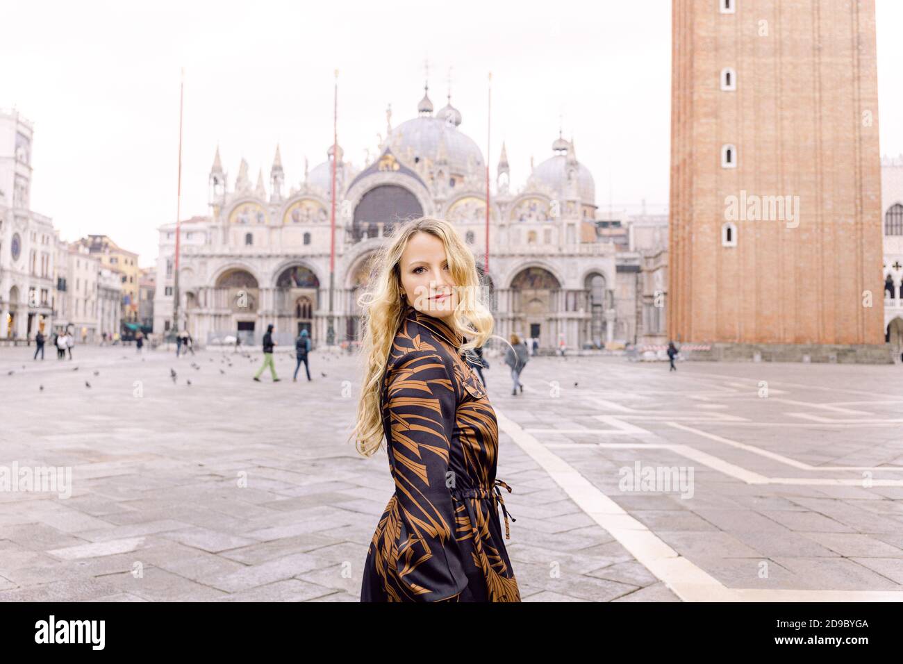 Blonde woman looking at the camera, in a long dark dress walking in Piazza San Marco, Venice, Italy Stock Photo
