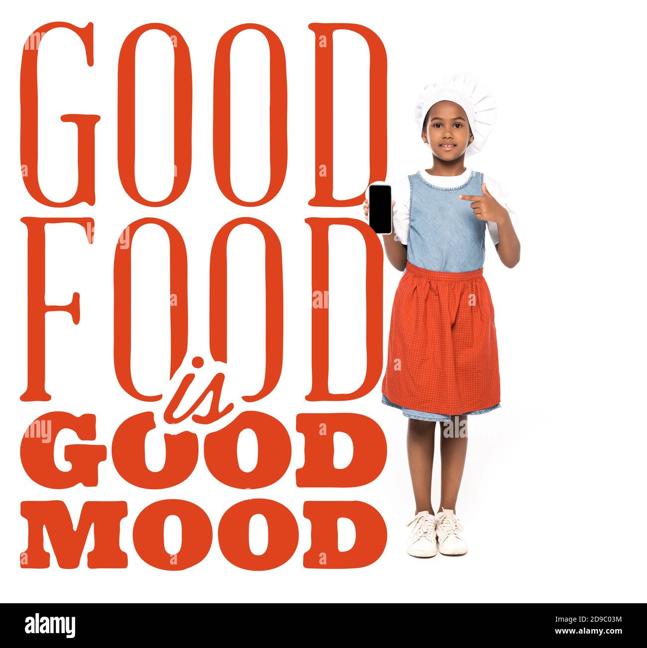 african american kid dressed in costume of chef pointing with finger at smartphone near good food is good mood lettering on white Stock Photo