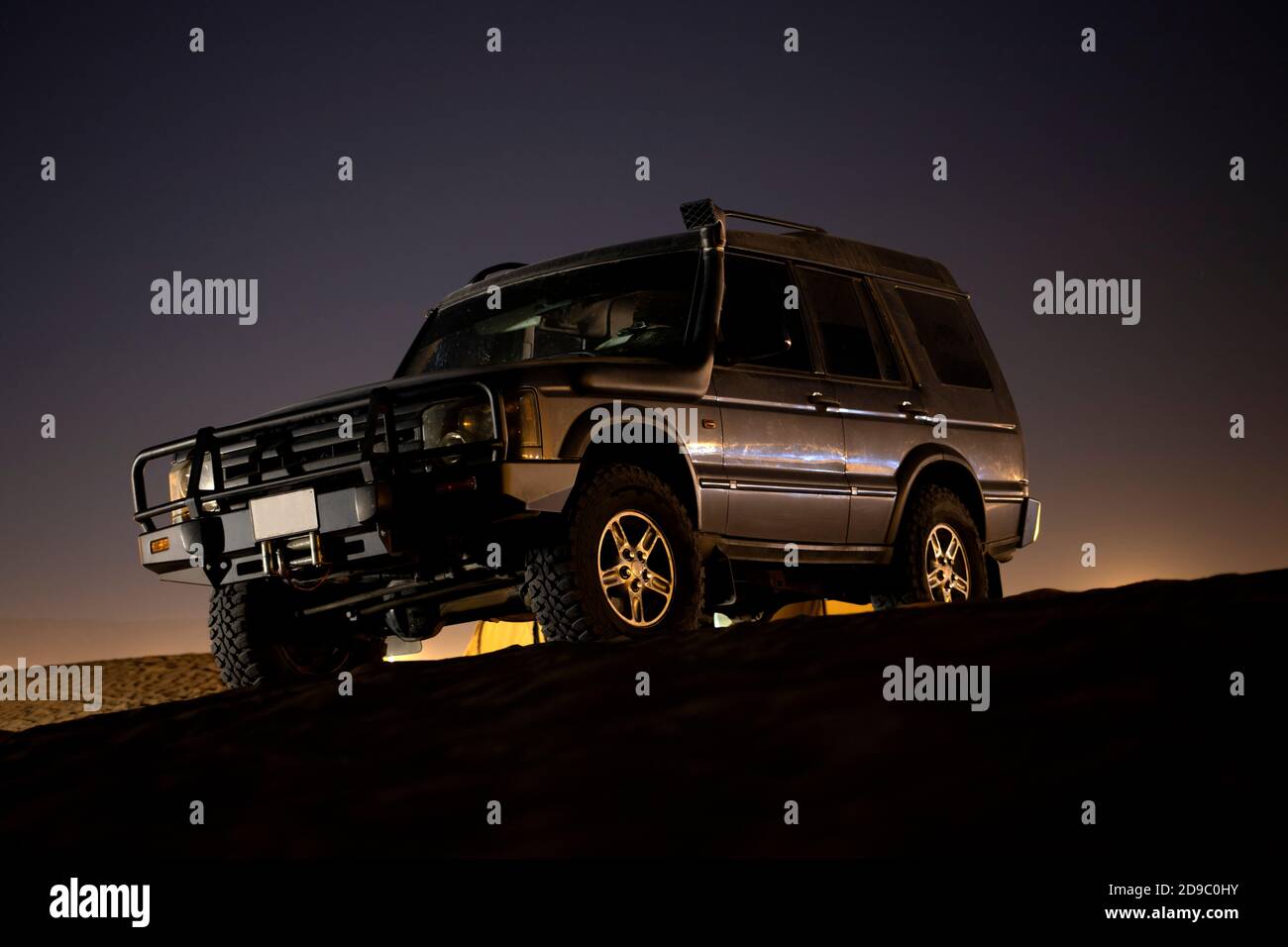 An unidentifiable SUV stands on a sand dune in the desert sunset in the United Arab Emirates Stock Photo
