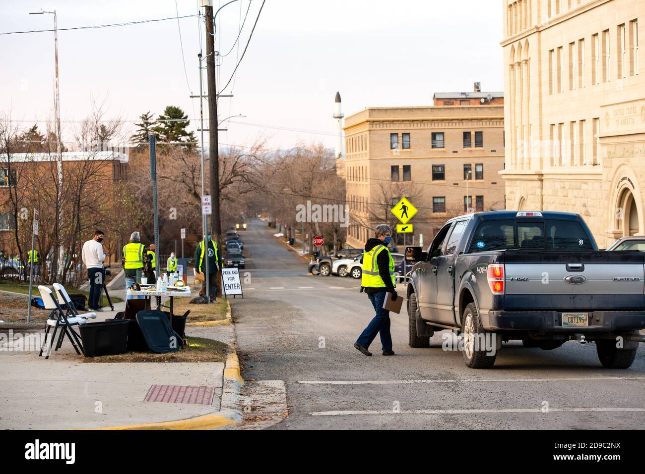 Helena, Montana / November 3, 2020: Election Day voting at polling station outside, woman poll worker in yellow vest wearing a mask for safety during Stock Photo
