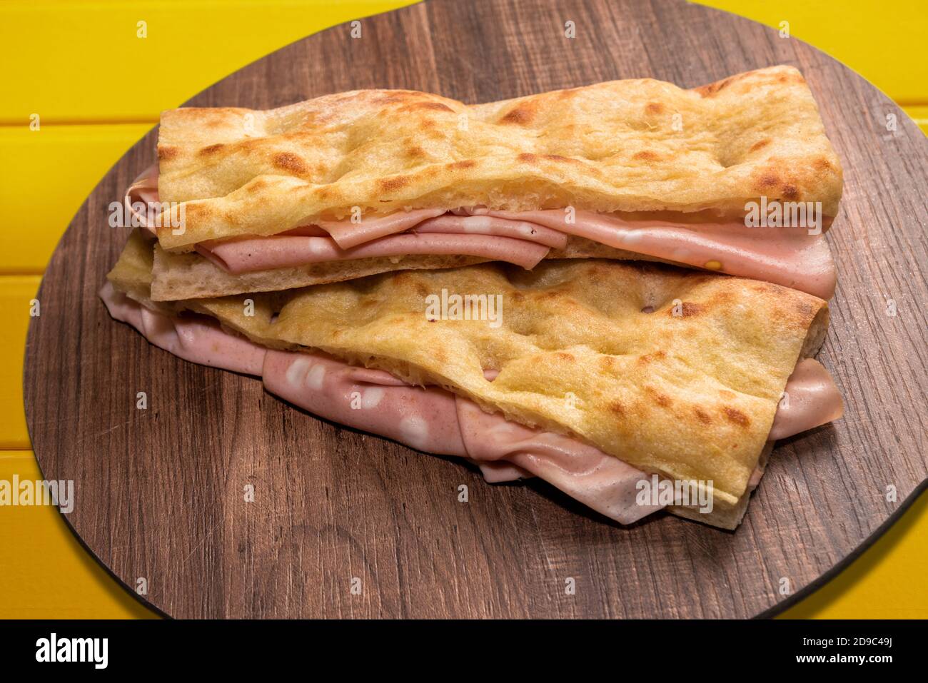 two focaccia bread sandwich filled with bologna mortadella on wooden cutting board and yellow background Stock Photo