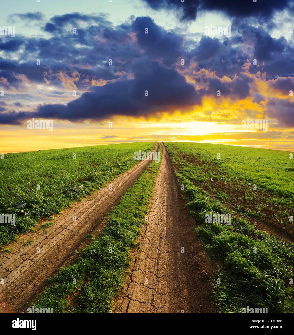 rural path uphill way to a dramatic sky at the sunset crossing a field of grass Stock Photo