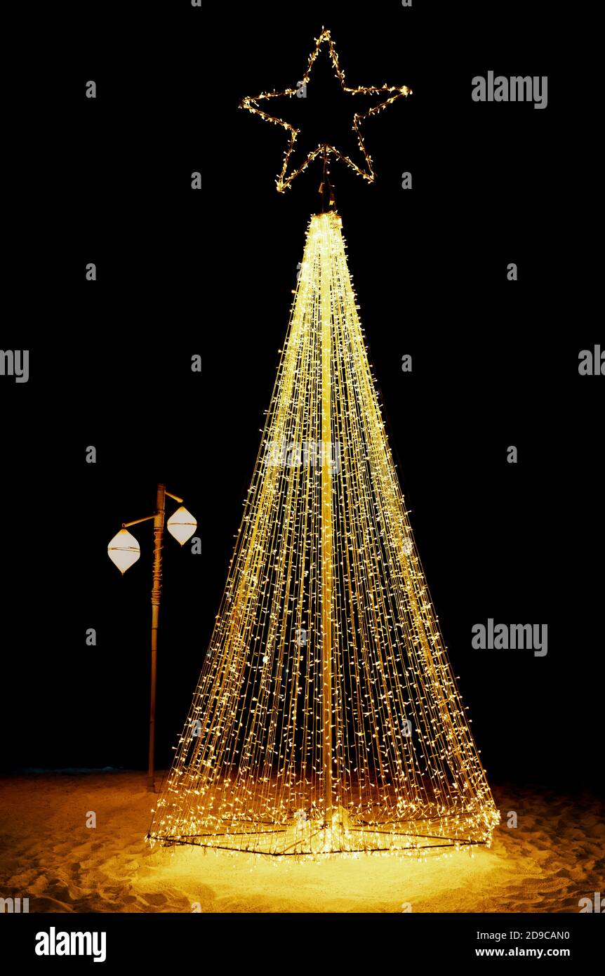 Bright shiny christmas tree made from string lights on sandy beach Stock Photo