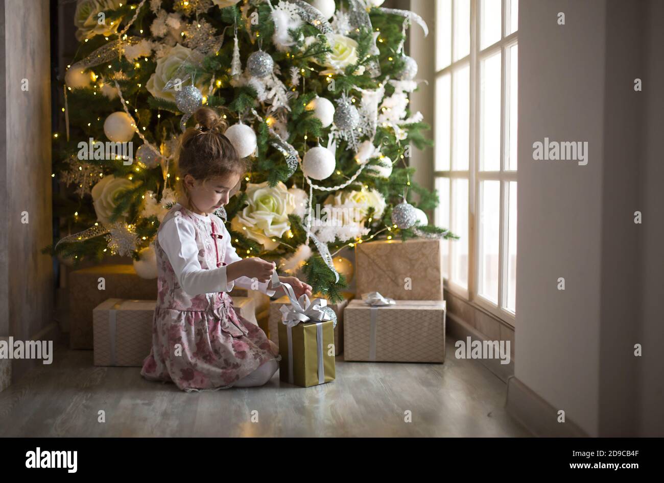 Little girl in beautiful dress is sitting under Christmas tree with ...