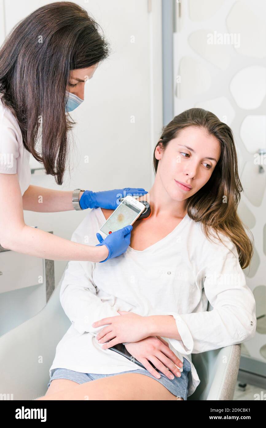 The doctor dermatologist examining client skin and mole with a special apparatus for diagnostic. Dermatoscopy procedure in the clinic. Concept of heal Stock Photo