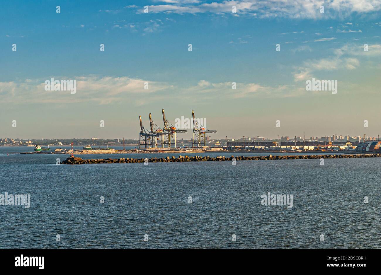 Montevideo, Uruguay- December 18, 2008: Cranes at shipping container terminal in port behind protective dam in blue Rio de la Plata water and under li Stock Photo