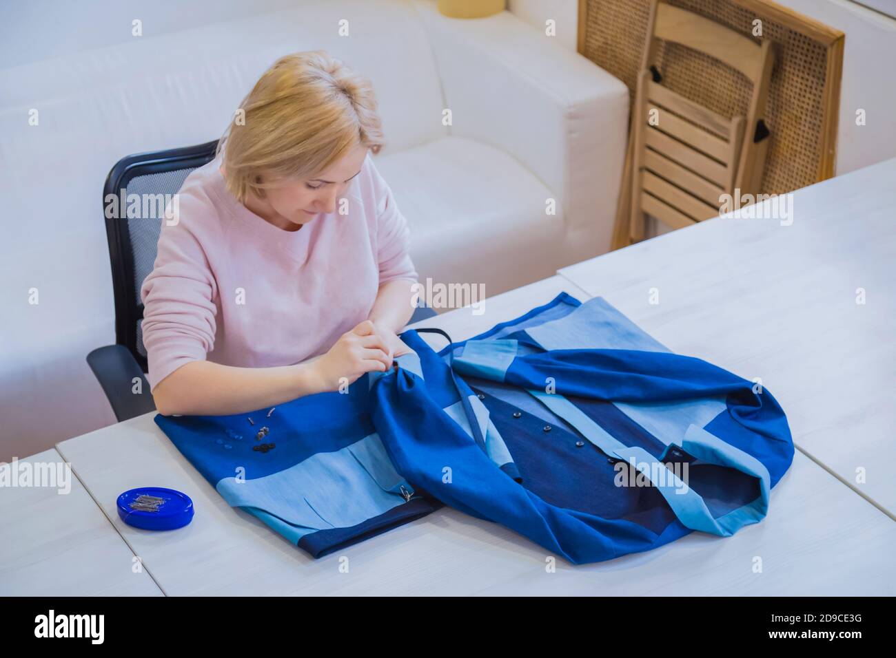 Portrait of professional tailor, designer sitting and measuring blue suit jacket for sewing at atelier. Fashion, clothing, small business, industry Stock Photo