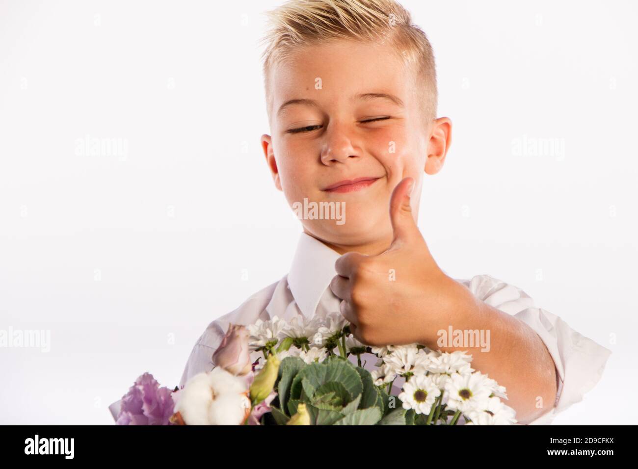 Cheerful blond fashionable boy gives bouquet and thumbs up on white studio background, delivery flowers, Spring Womens Day Stock Photo