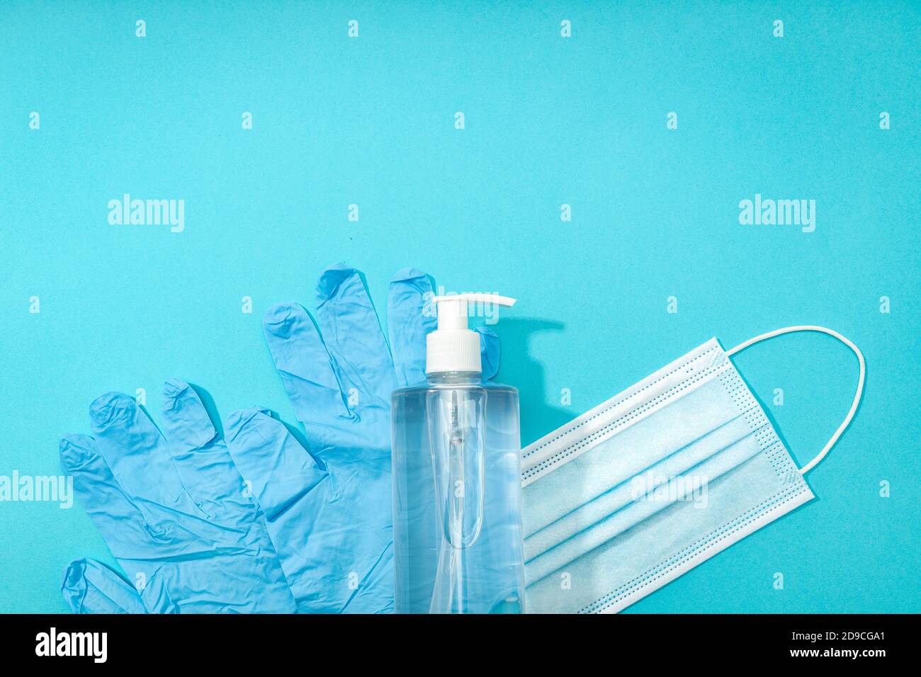 Covid-19 coronavirus protection or prevention concept. Medical face mask, gloves and hand sanitizer on blue background. Top view. Copy space Stock Photo