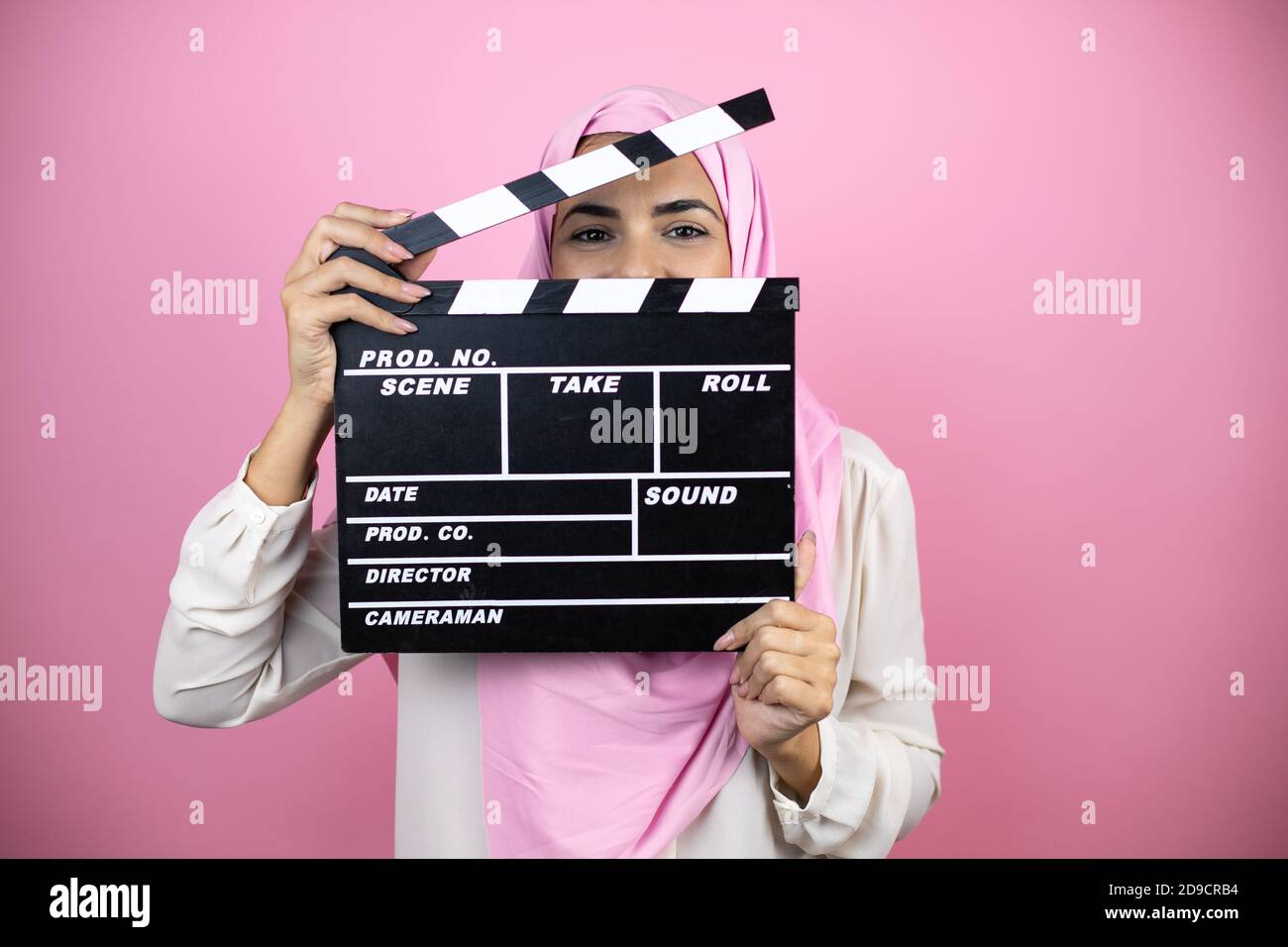 Young beautiful arab woman wearing islamic hijab over isolated pink background holding clapperboard very happy having fun Stock Photo