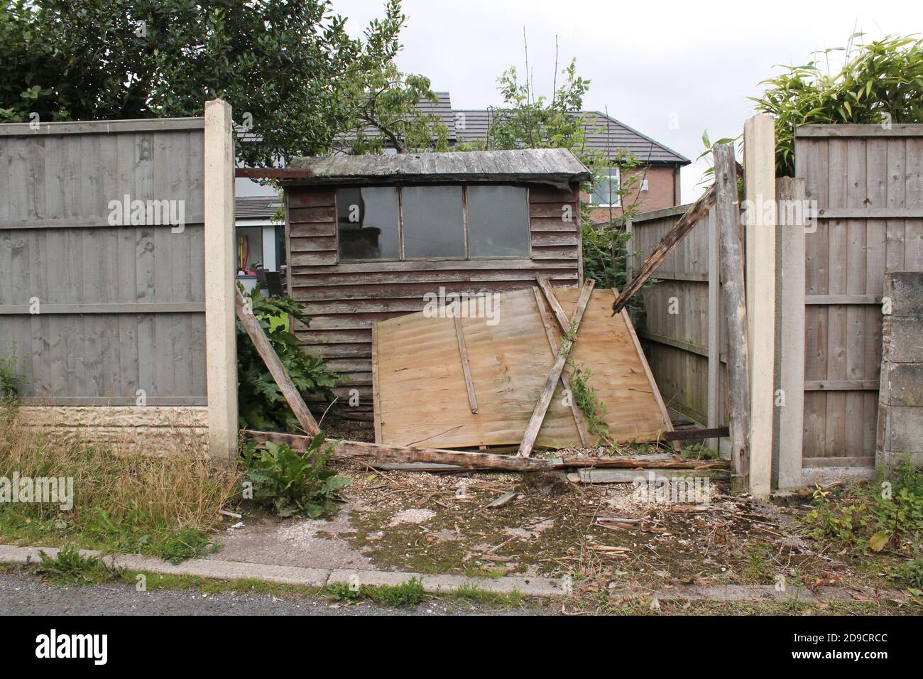 Wind damage fence panel at the back of a garden, revealing a ram shackled shed Stock Photo