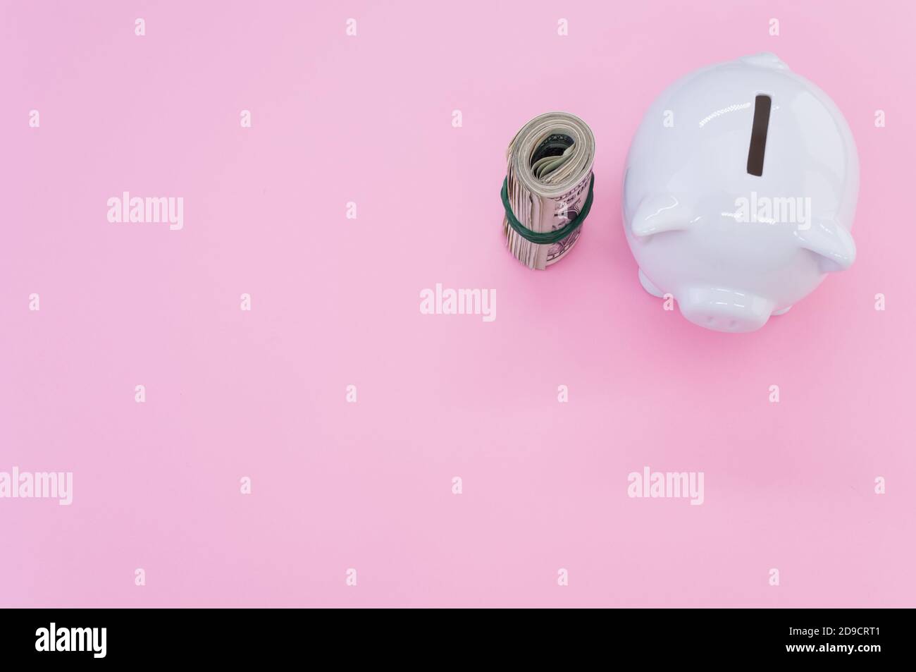 High angle shot of dollar bills and a piggy bank on a pink surface ...