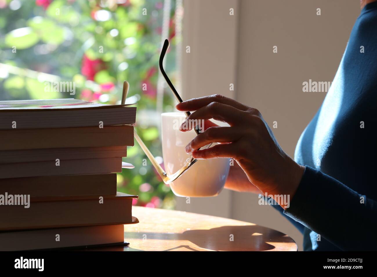Woman with eye glasses sitting at table with a pile of books Stock Photo