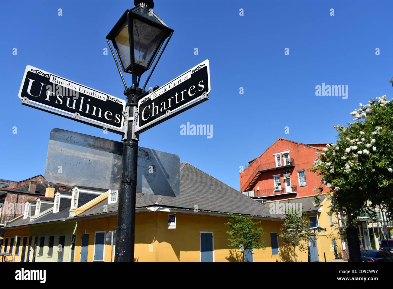 A traditional street sign post with a lamp on top points the way for Ursulines Street and Chartres Street in the historic French Quarter, New Orleans. Stock Photo