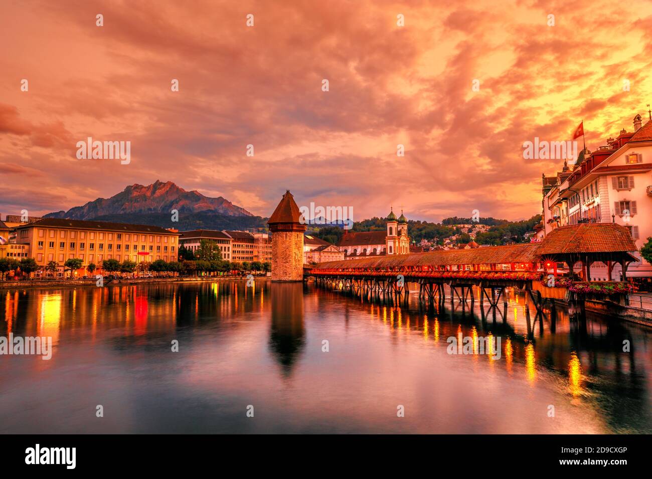 Mount Pilatus mountain overlooking the skyline of Lucerne town of Switzerland. Dusk cityscape with city lights and Chapel Bridge with Water Tower on Stock Photo