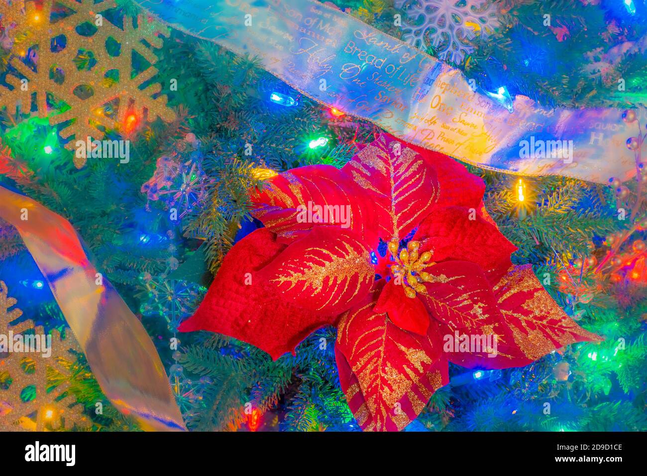 Colored lights fill a Christmas tree with Poinsettias and snowflakes between ribbon garlands. Stock Photo