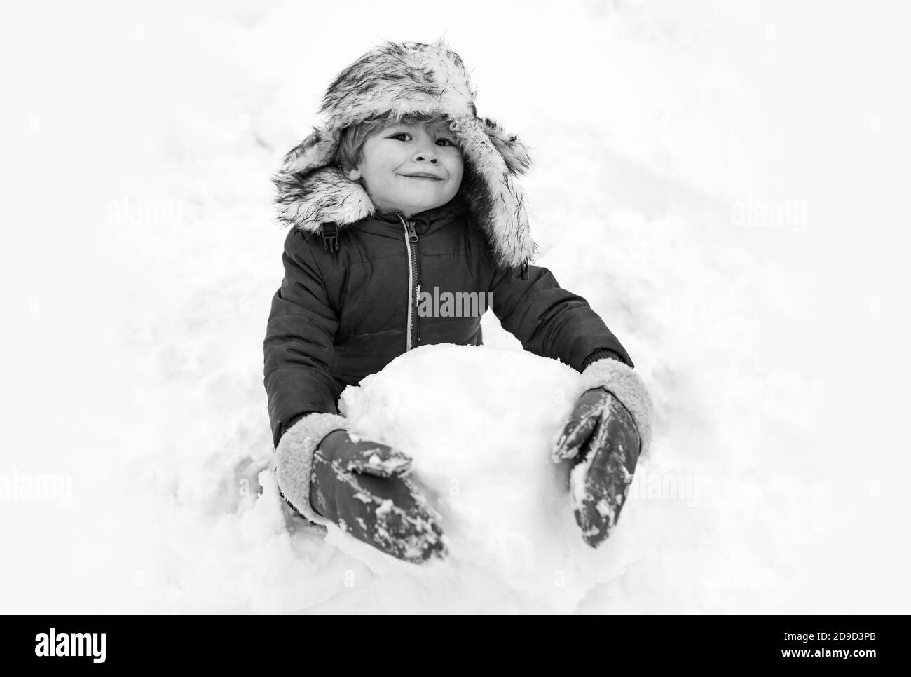 Snowman and funny child the friend is standing in winter hat and scarf with red nose. Joyful kid Having Fun with snowman in Winter Park. Winter Stock Photo