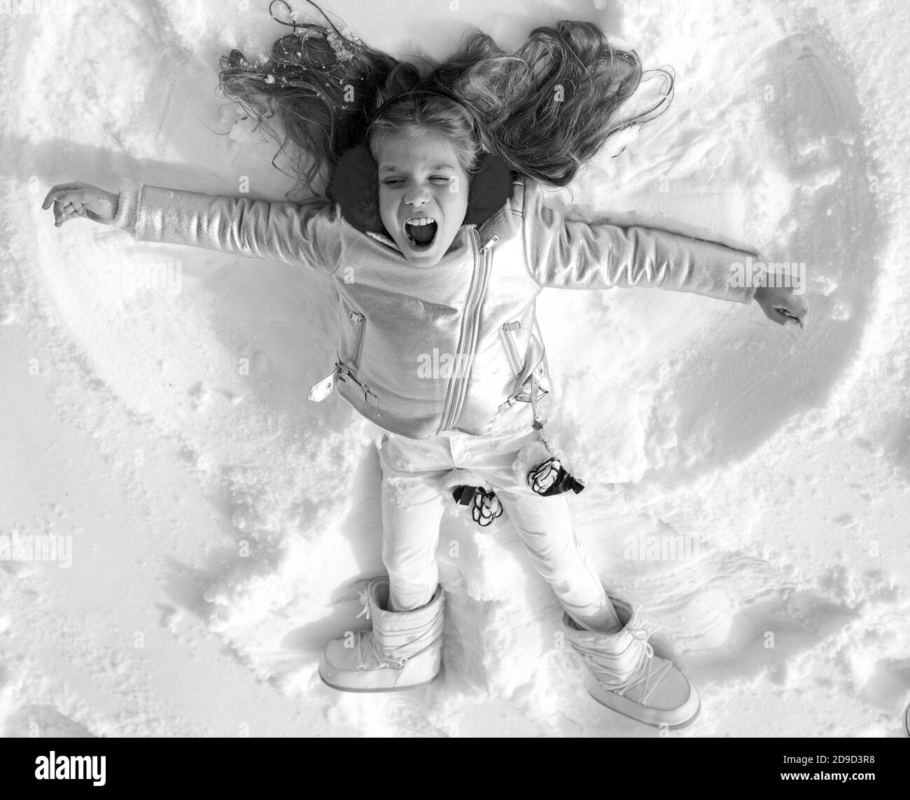 Girl on a snow angel shows. Smiling child lying on snow with copy space