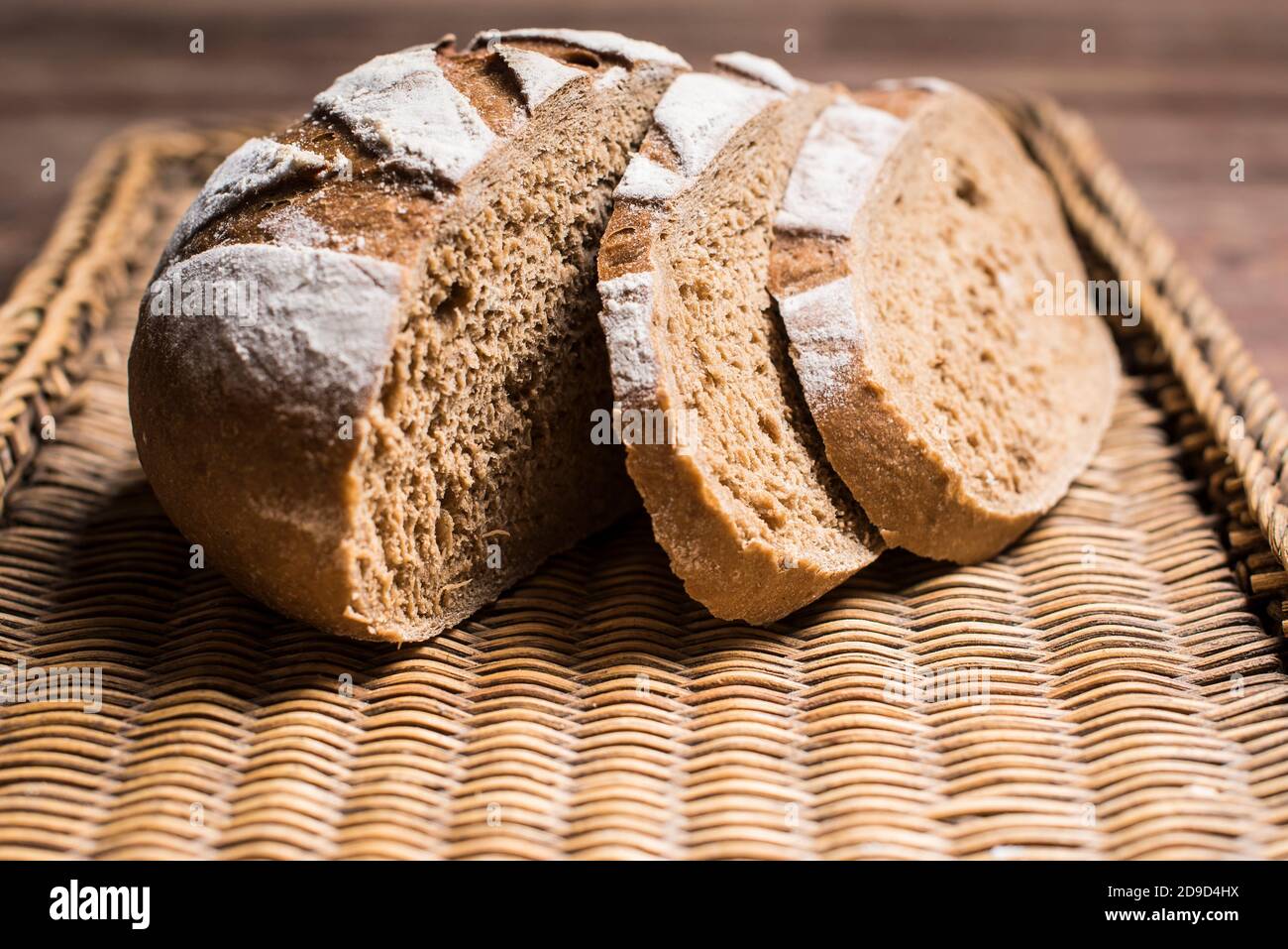 Loaf of brown bread with two slices cut on a brown wicker tray Stock Photo