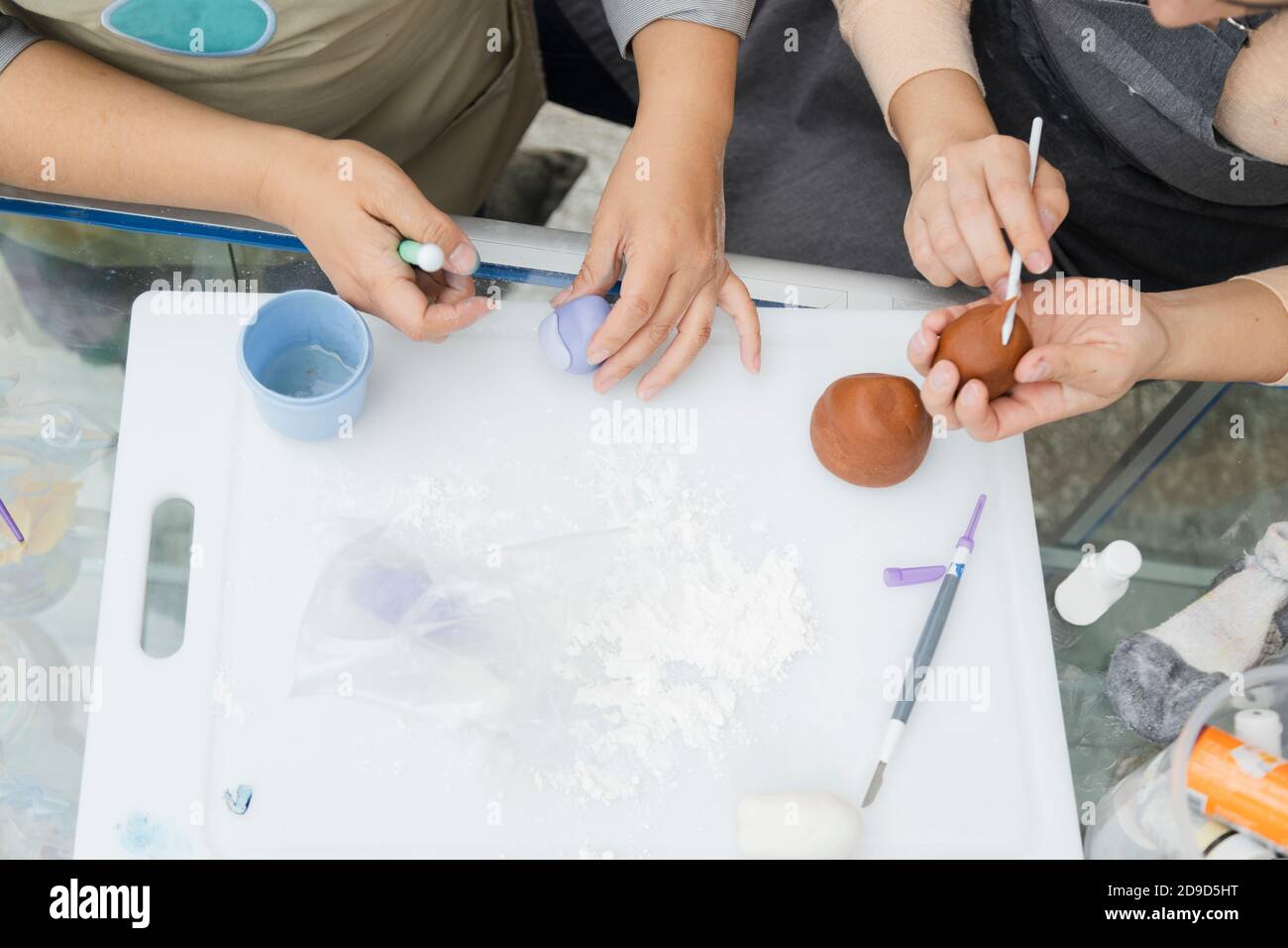 Top view of the hands of women pastry chefs working with fondant to decorate a cake - hands molding clay with tools and coloring - women artisans Stock Photo