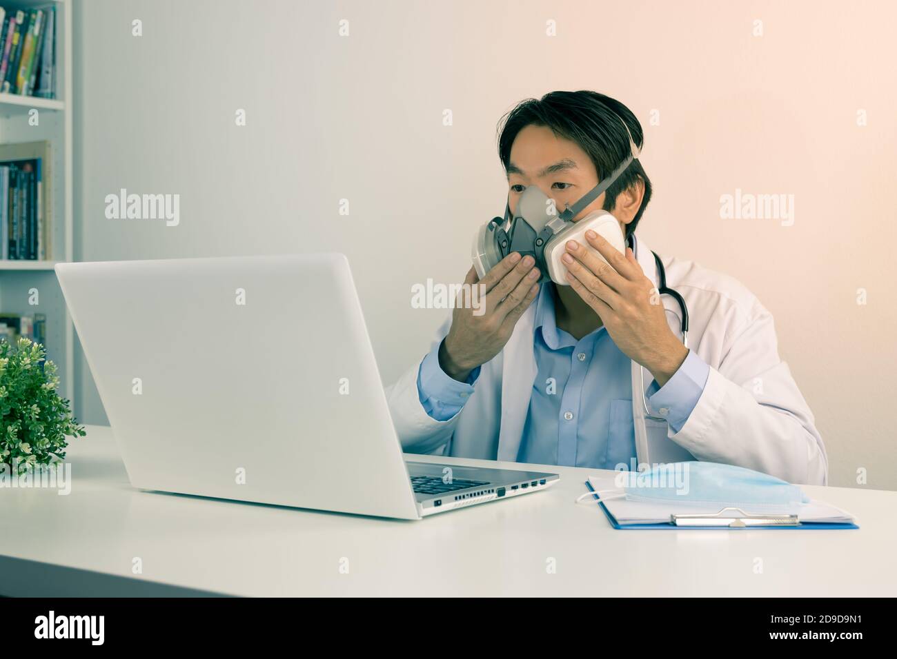 Young Asian Doctor Man in Lab Coat or Gown with Stethoscope Demonstrate Filter Mask Using with Patient Via Laptop Computer in Office in Vintage Tone Stock Photo