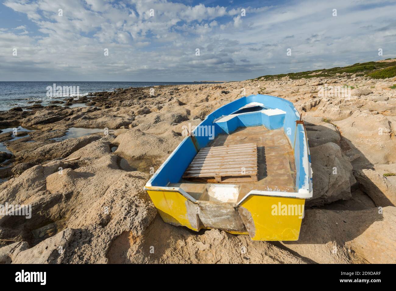 yellow wooden boat stranded on stony shore with dramatic cloudy sky after storm . Menorca, Spain Stock Photo