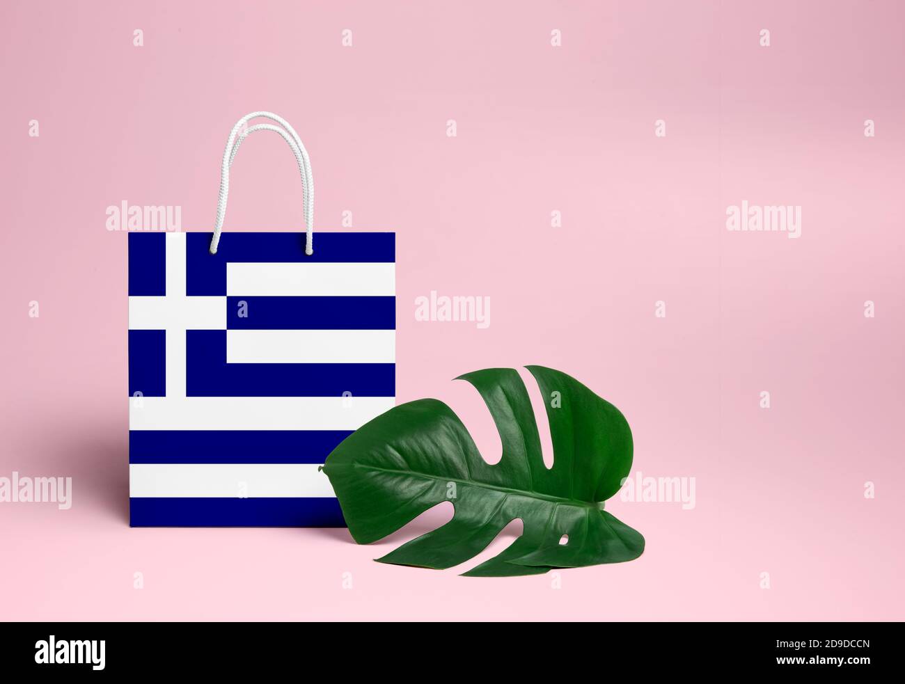 Greece shopping concept. National cardboard shopping bag with monstera leaf and pink background. Online shopping theme. Stock Photo