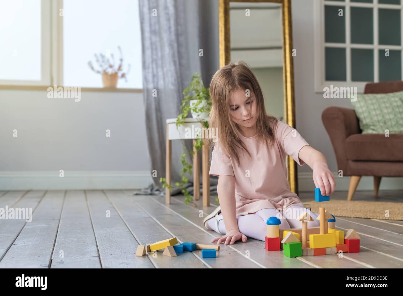 Cute girl plays on the floor with a wooden constructor Stock Photo