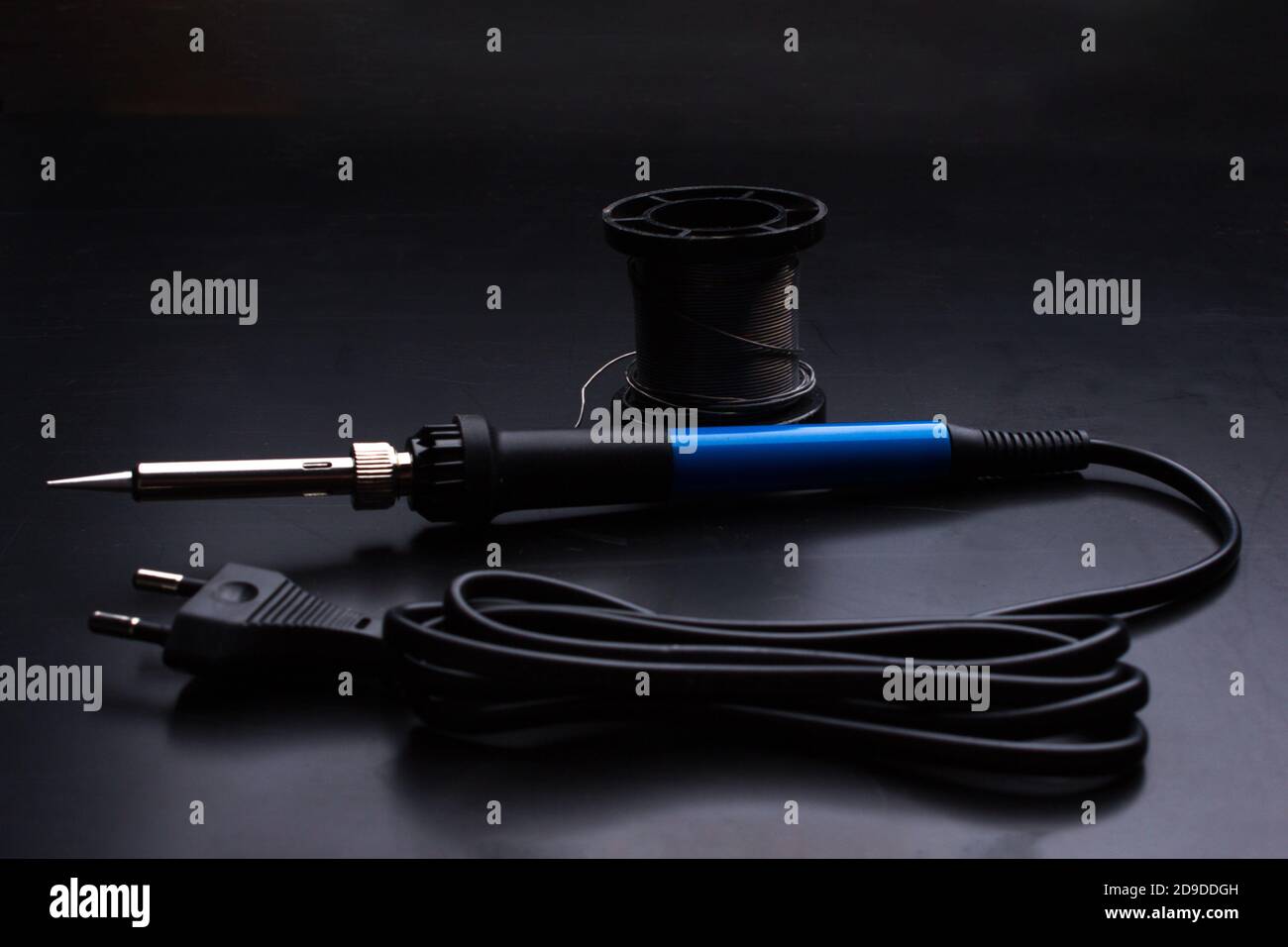 A soldering iron with a blue handle and a coil of solder on the old