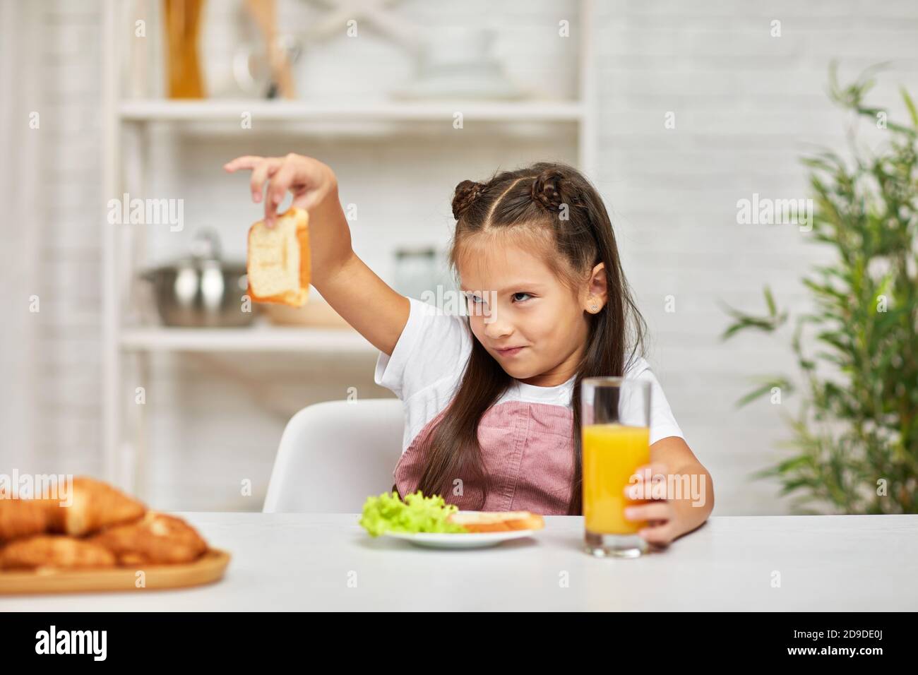 the child does not want to have breakfast. little girl looks at the sandwich with disgust Stock Photo