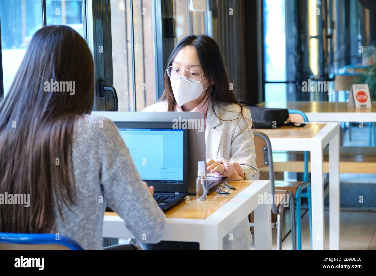 Two female students wearing face masks working on their computers in a restaurant. New normal in restaurants. Coronavirus pandemic. Stock Photo