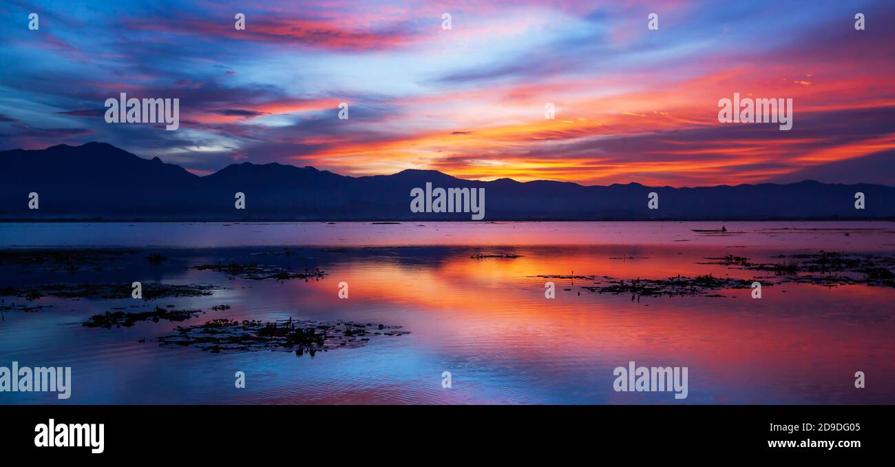 Dramatic sunset sky with clouds over the lake and mountains in the backgrounds, colourful clouds and sky reflection on the lake. Phayao, Thailand. Stock Photo