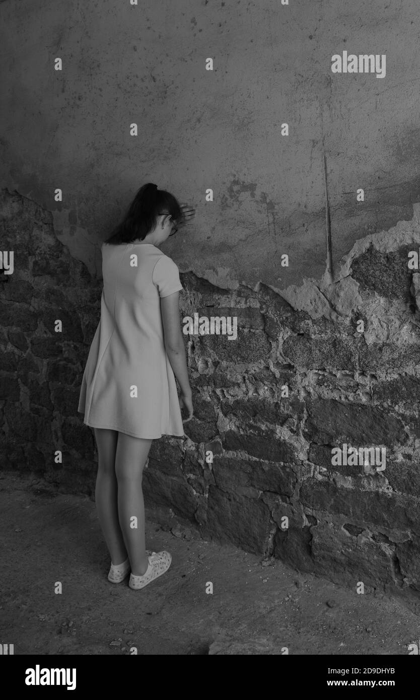 Young girl teenager with depression stands leaning against an old brick wall, vertical frame, copy space Stock Photo