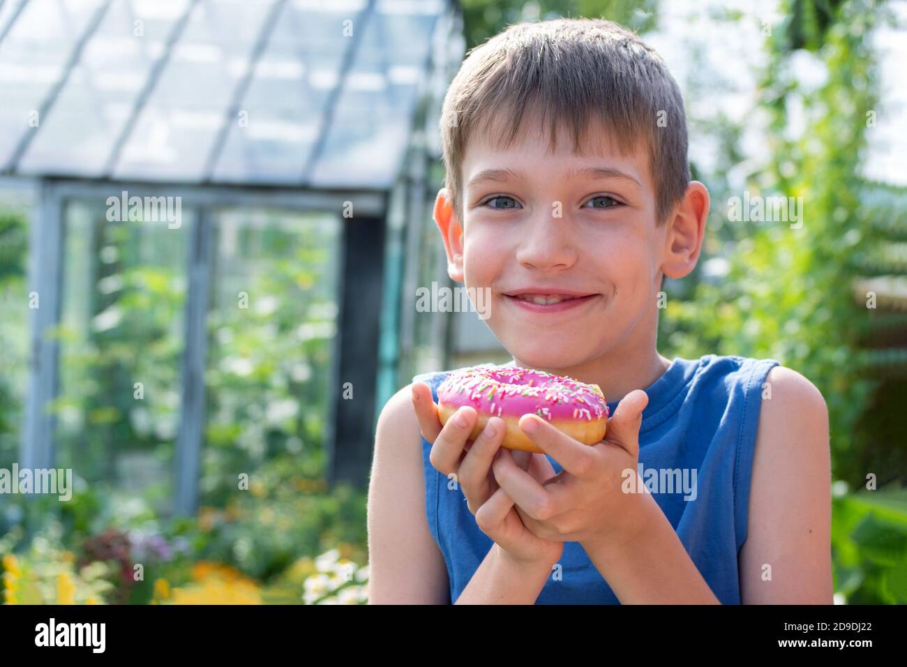 Happy child holding a pink donut in the park. The child refuses to eat healthy food. Unhealthy food concept Stock Photo