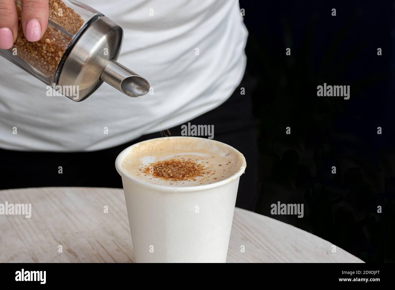 Close-up of a female hand pouring brown sugar from a dispenser into a ...