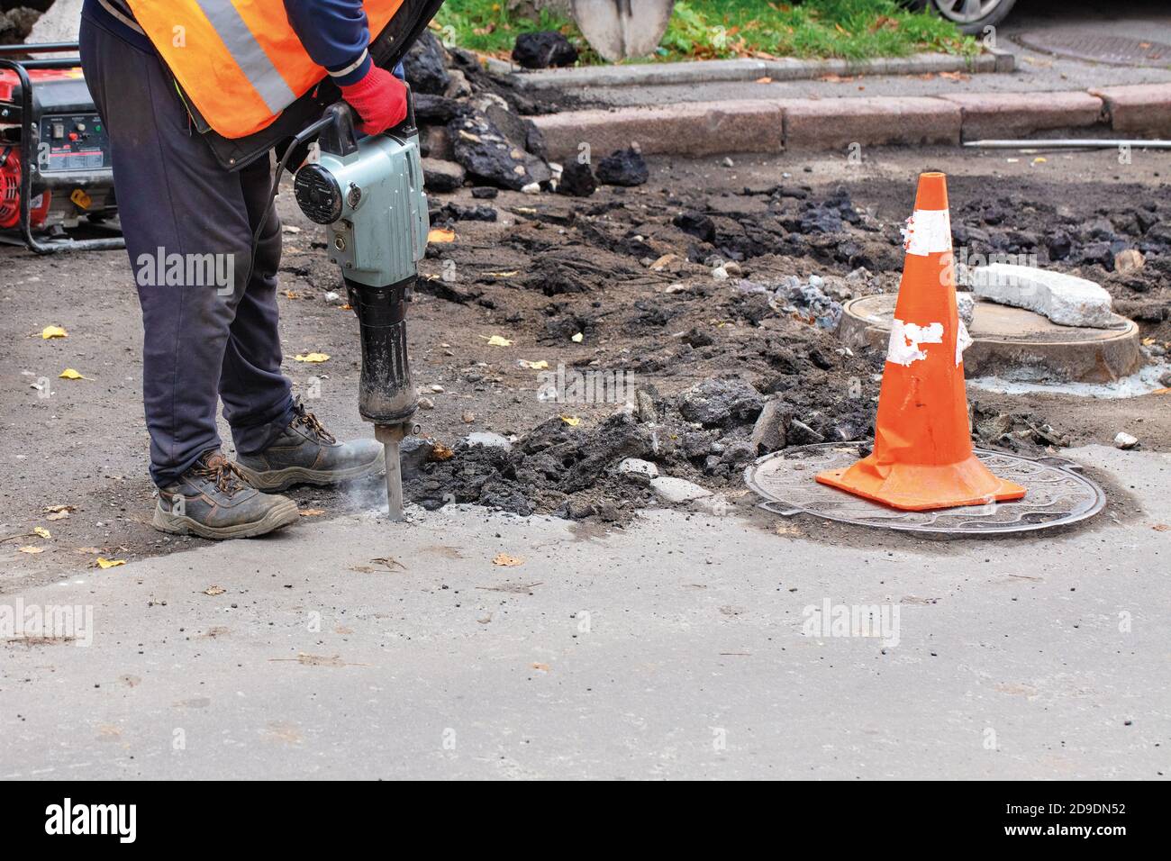 A road dressed in reflective clothing, uses an electric jackhammer to rip old asphalt off the road and uses a gasoline generator, copy space Stock Photo -