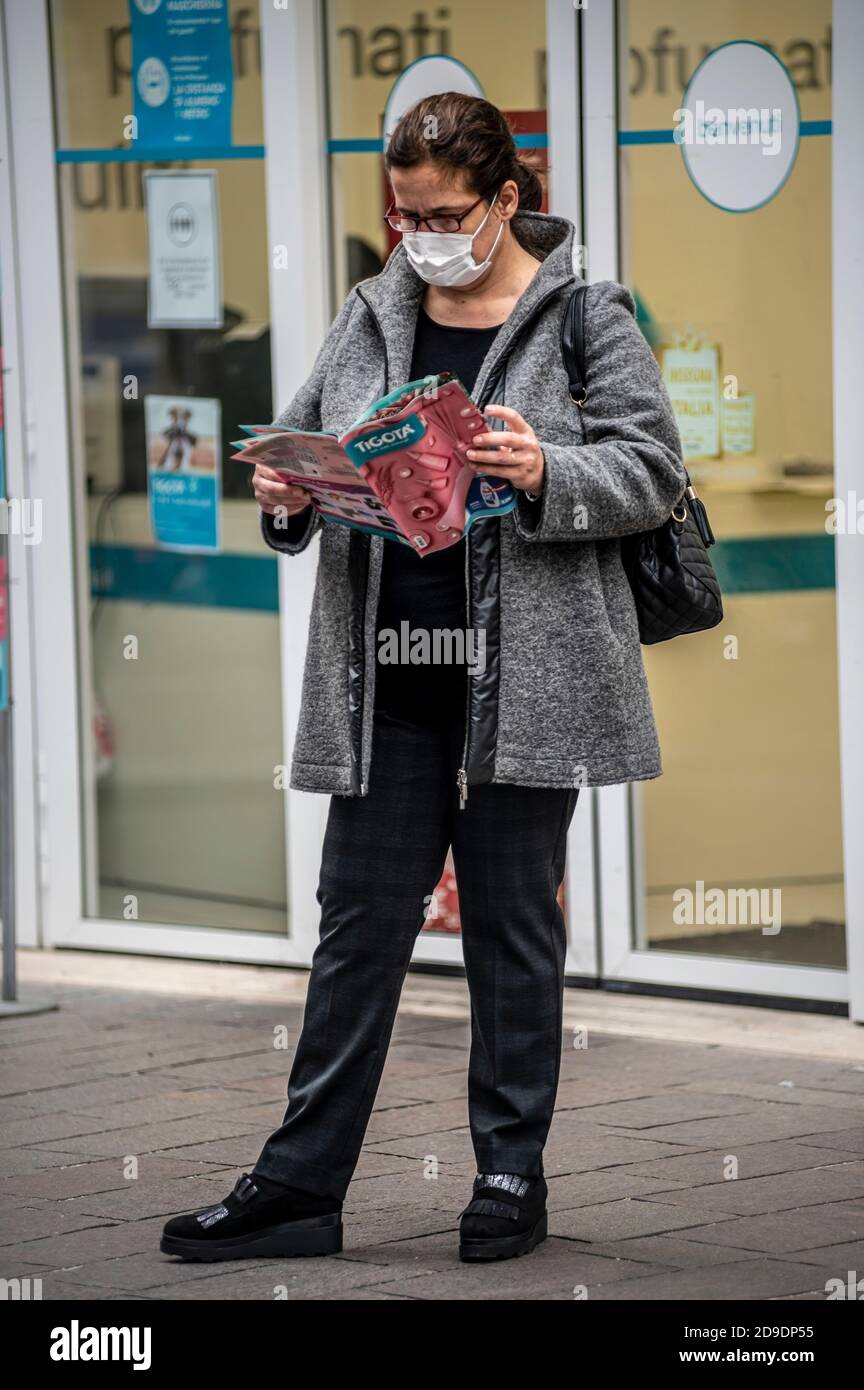 terni,itali november 05 2020:woman wearing medical mask in front of a shop looking at a brochure Stock Photo