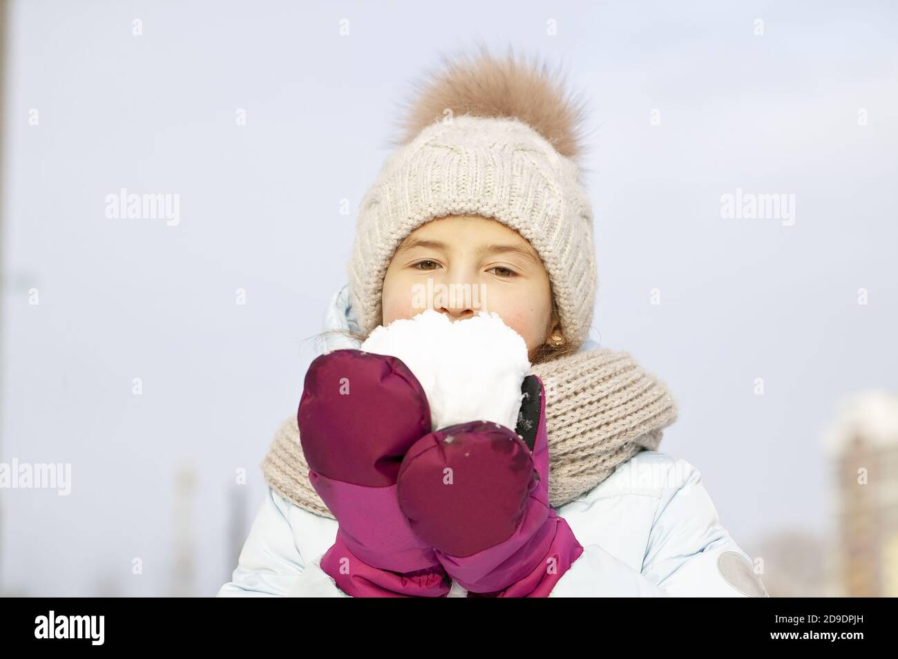 Winter portrait of a beautiful girl in a winter knitted hat. Girl holding snow. Stock Photo