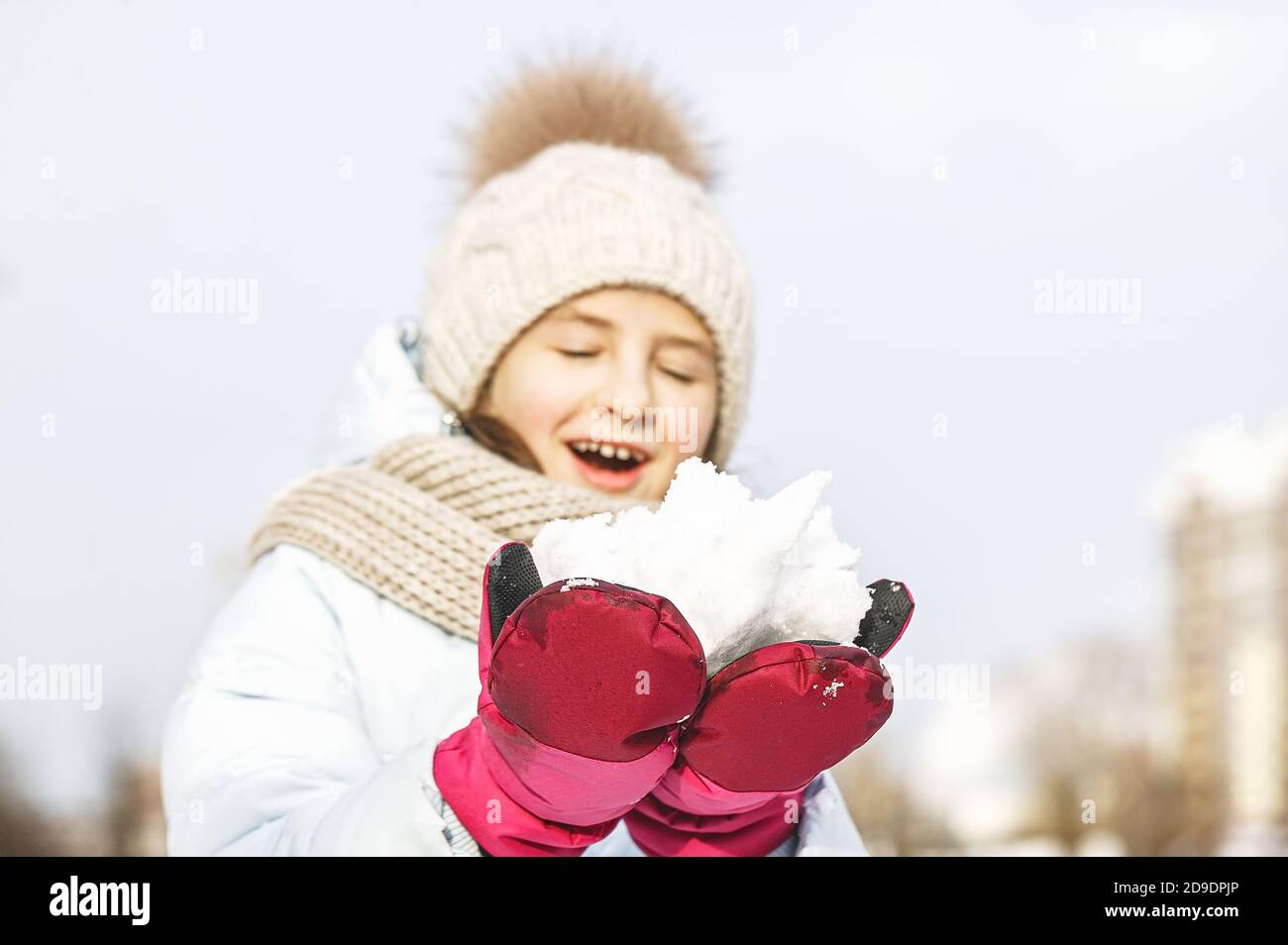 Winter portrait of a happy beautiful girl in a winter knitted hat. Girl holding snow. Lifestyle Stock Photo