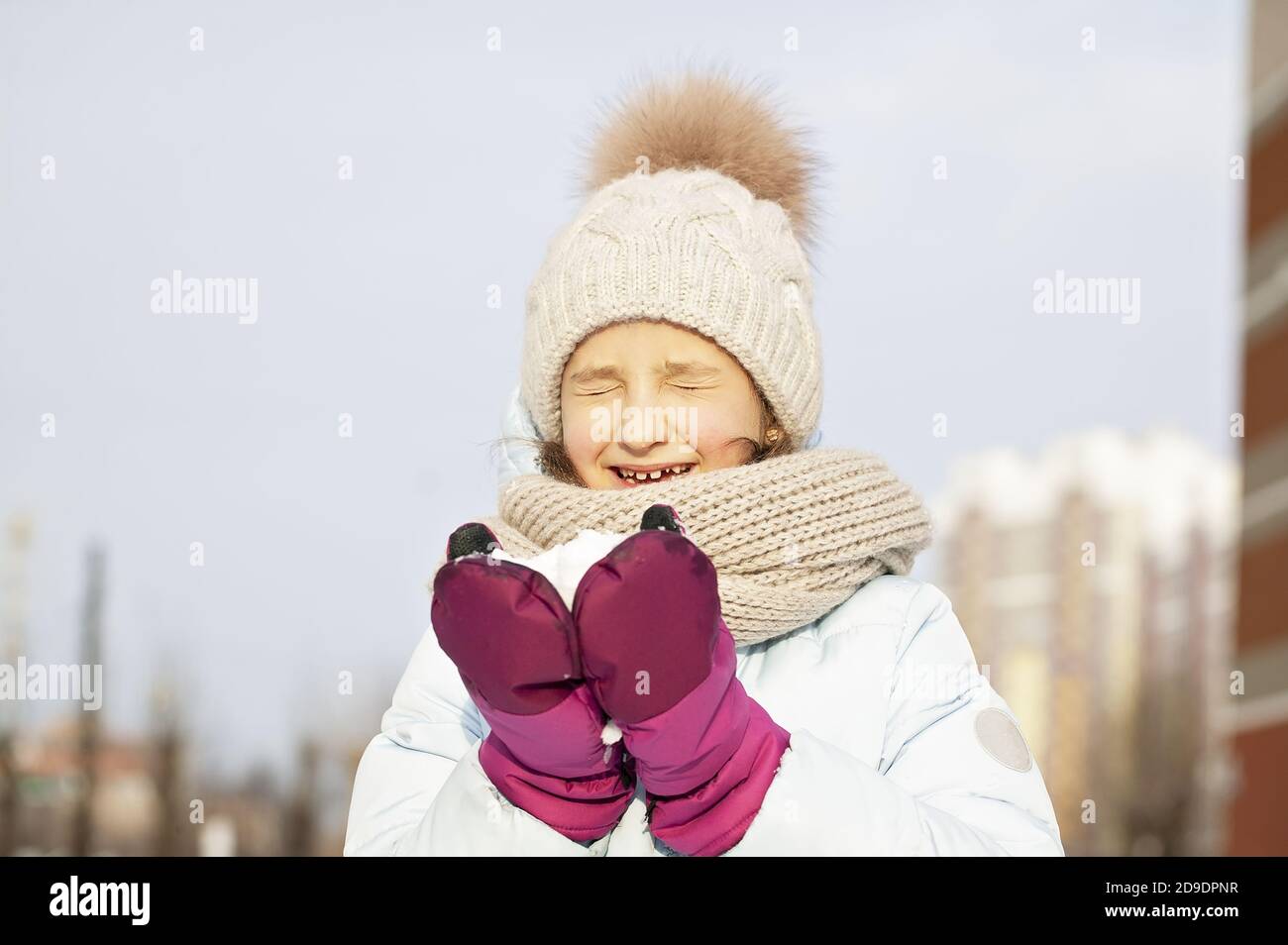 Winter portrait of a happy beautiful girl in a winter knitted hat. Girl holding snow. Lifestyle Stock Photo