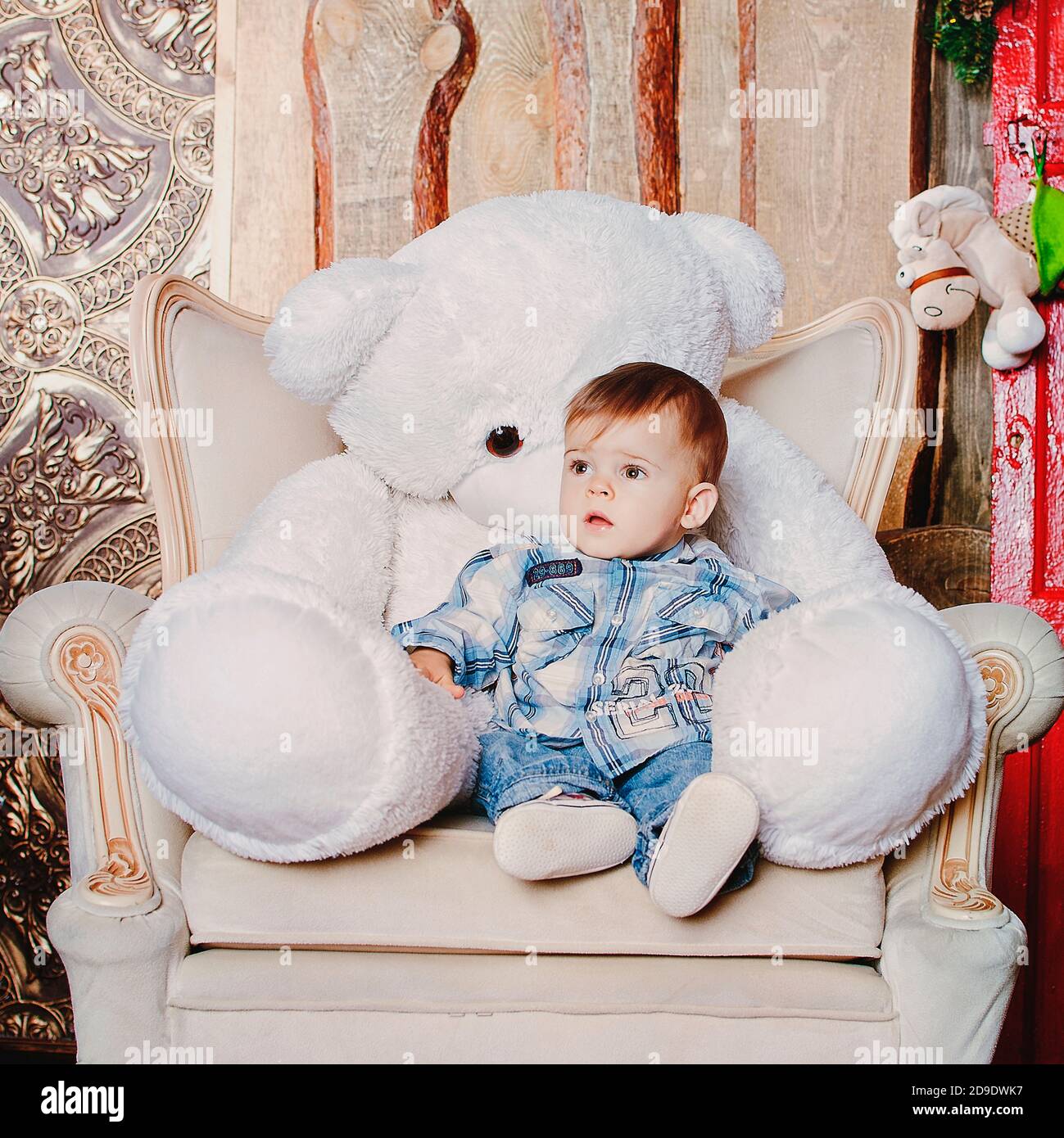 Cheerful and happy little boy sitting with his bear toy on the chair against Christmas decorations. Christmas traditions. Stock Photo