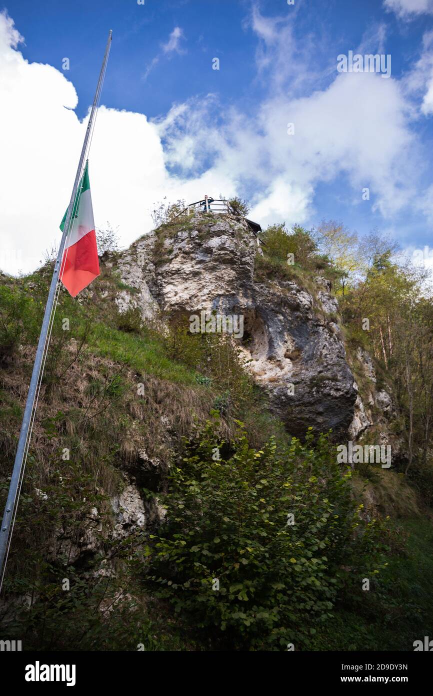 Italian flag on a pole with a rock and cloudy blue sky in the background Stock Photo