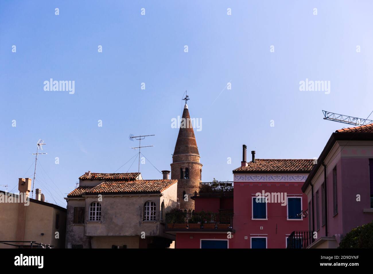Protruding bell tower behind buildings with blue sky in the background. Caorle Italy Stock Photo