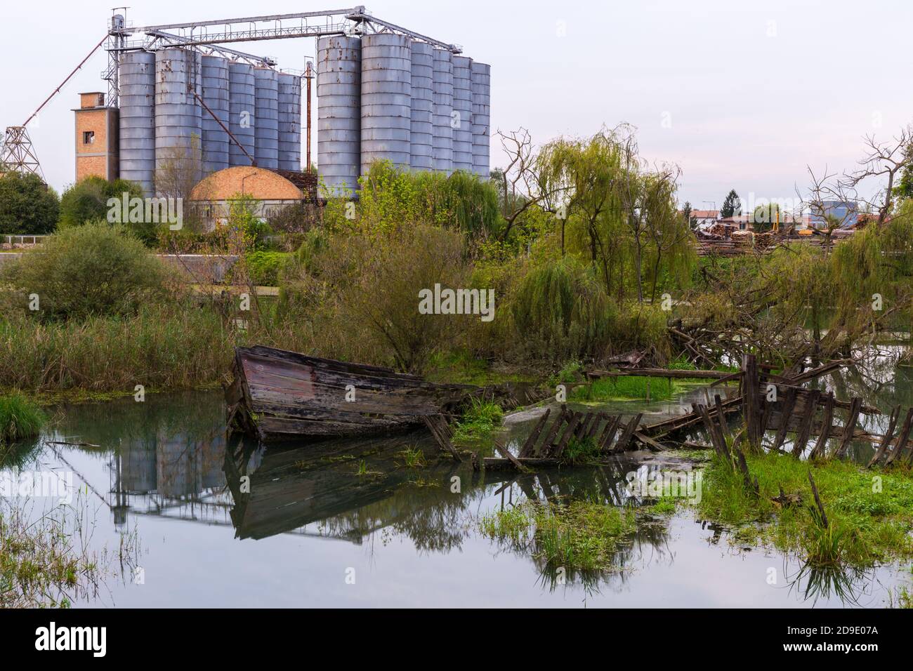 Historical cemetery of sunken wooden shipwrecks in the water in the Sile river called Burci cemetery with an abandoned factory with silos in the backg Stock Photo