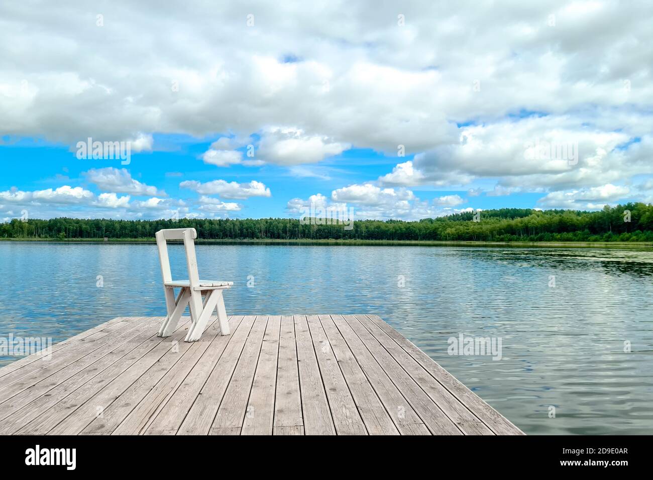 White wooden empty chair at the lake dock facing beautiful view. Stock Photo